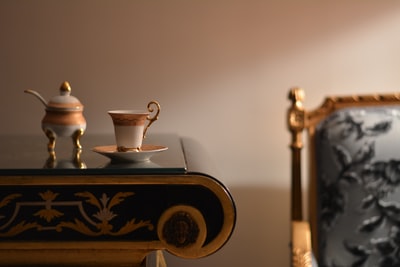 The teapot on the brown wooden desk near white and gold ceramic cups and saucers
